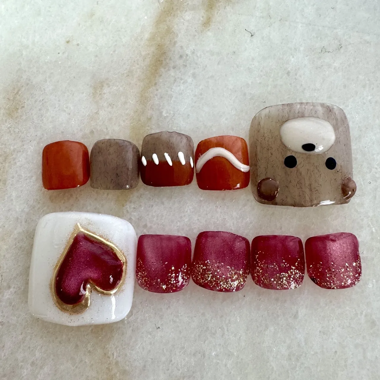 オレンジとブラウンにクマの顔、ホワイトとボルドーにハートモチーフを合わせたフットネイル